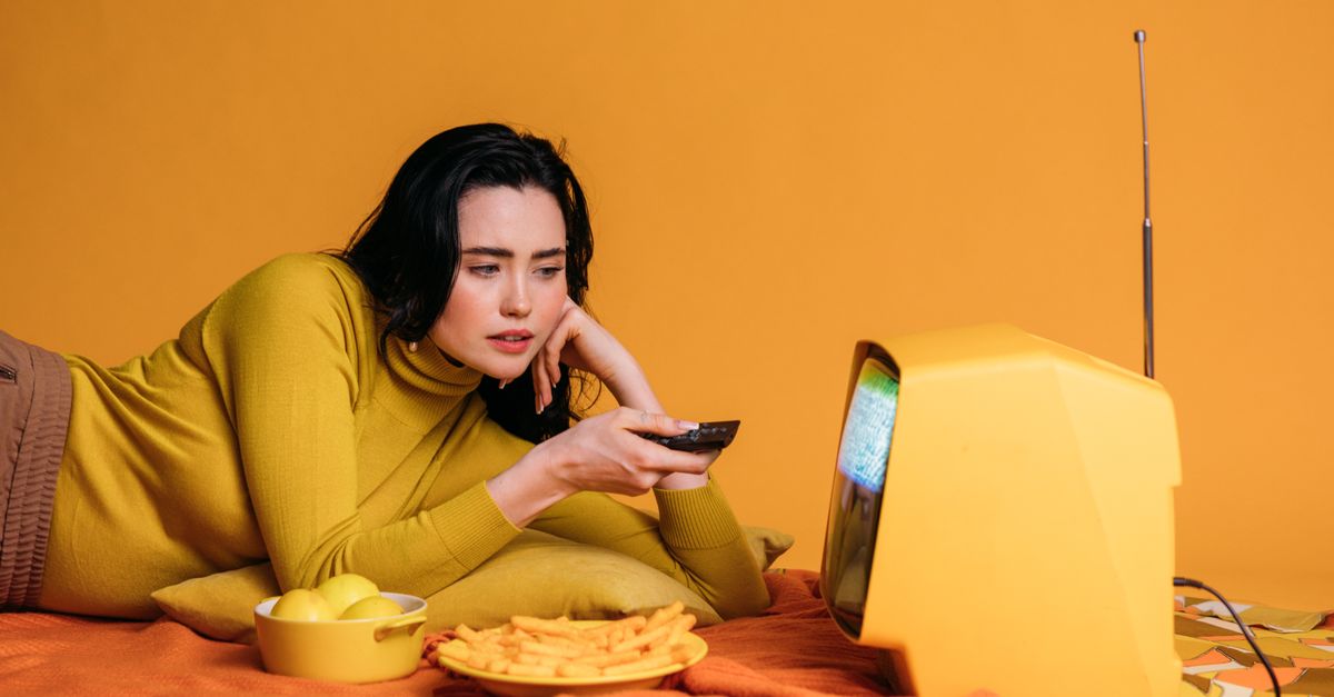 Femme détendue mangeant des chips en regardant une télévision ancienne dans le salon.