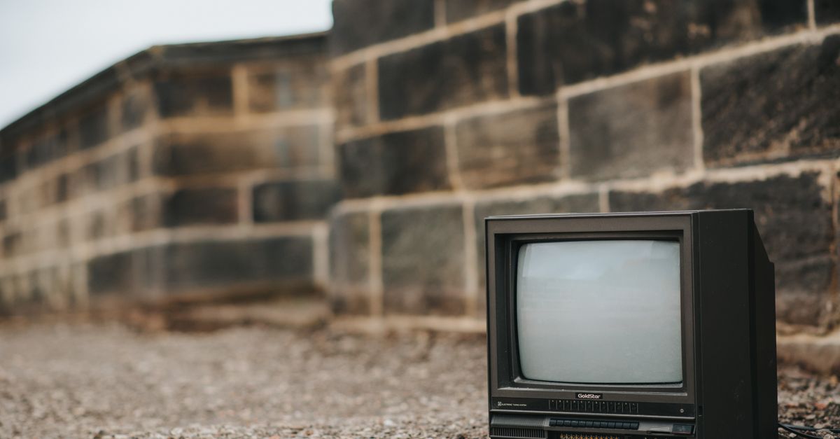 Vieille télévision noire posée au sol près d’une clôture en béton, en extérieur urbain