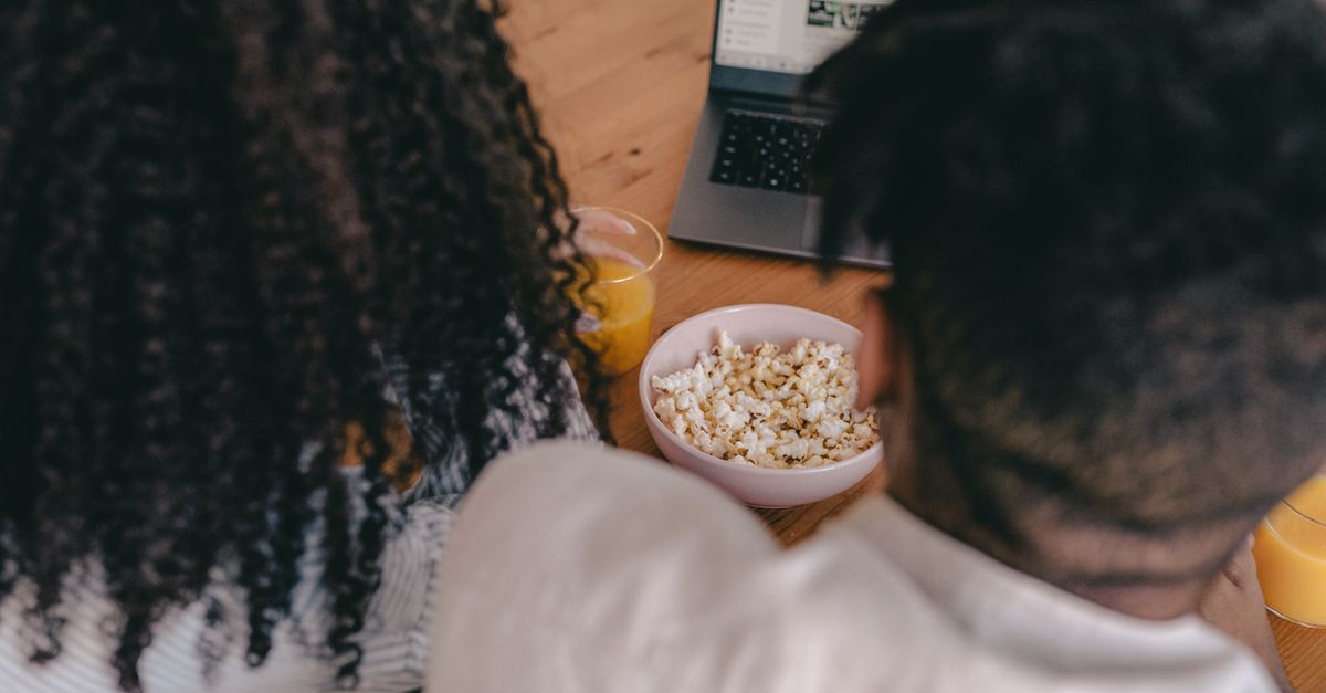 Couple partageant du pop-corn devant un ordinateur portable, atmosphère conviviale et détendue