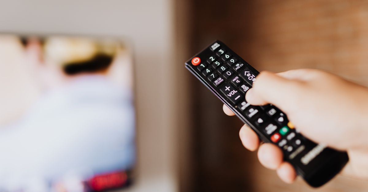 Gros plan sur une main dirigeant une télécommande devant un écran flou.