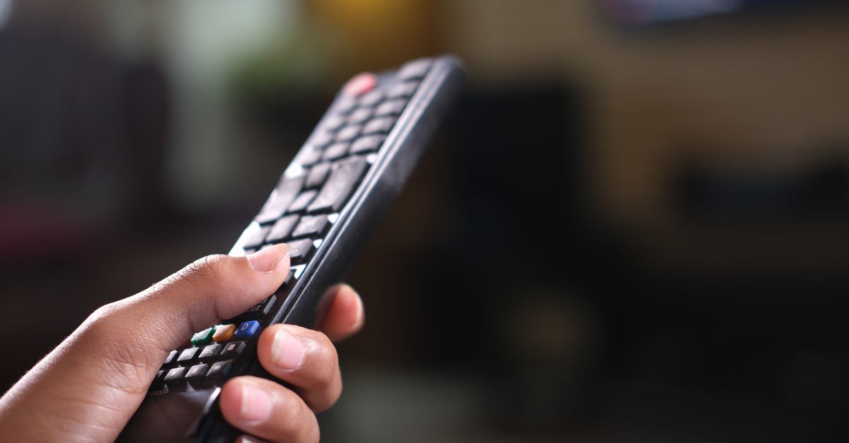 Main tenant fermement une télécommande de télévision, boutons bien visibles en intérieur.