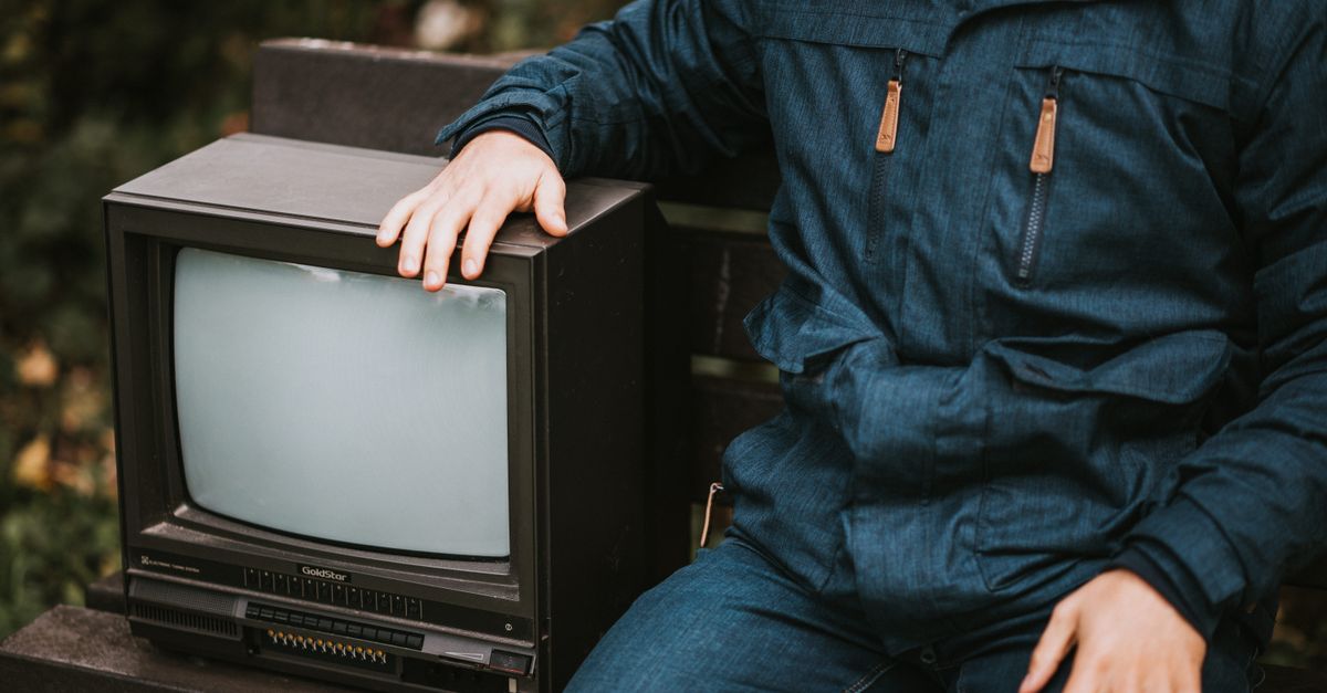 Homme assis sur un banc en bois regardant une petite télévision rétro dans un parc