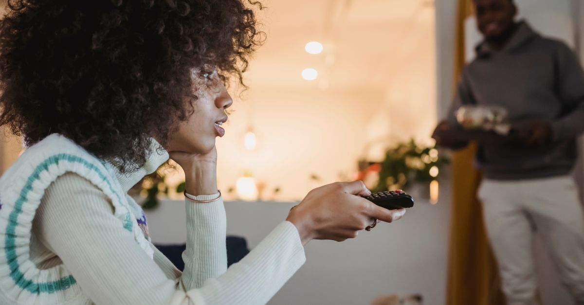 Jeune femme concentrée utilise une télécommande pour changer de chaîne à côté de son compagnon souriant